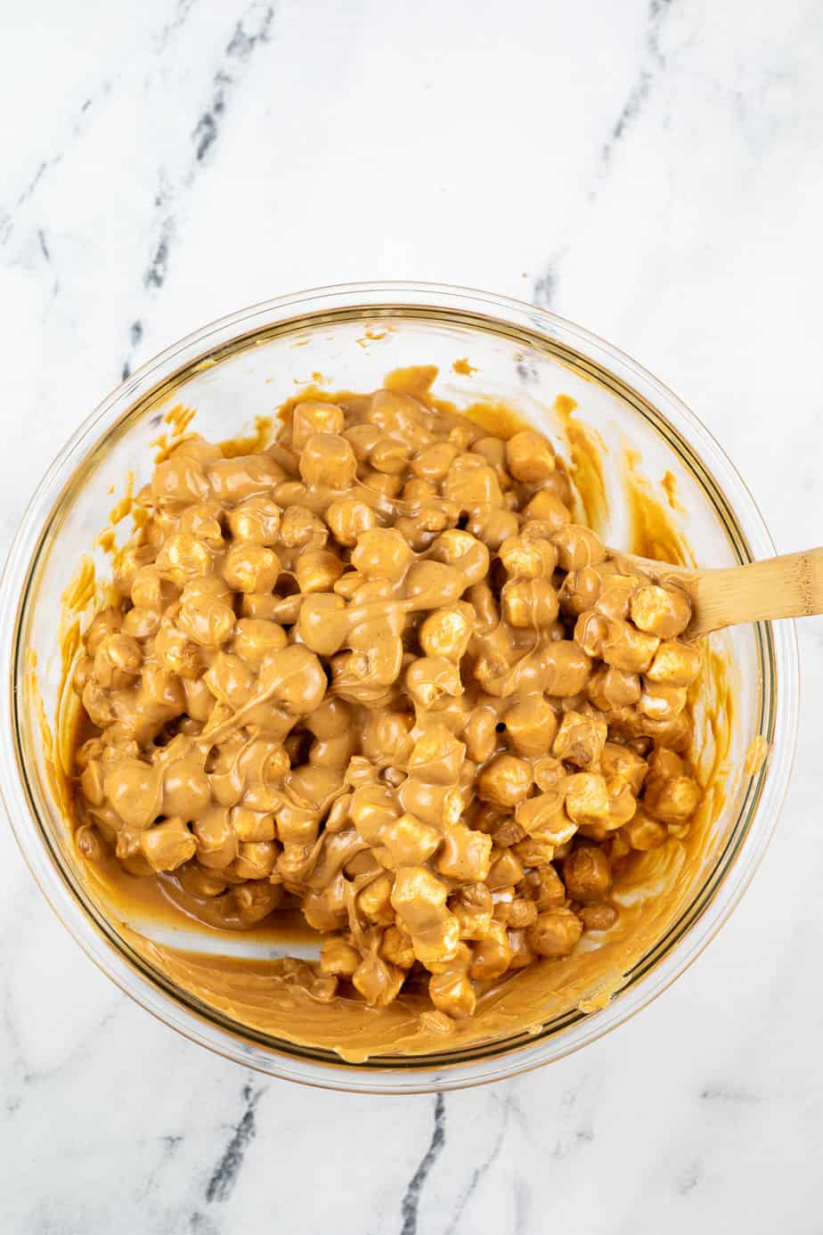 Marshmallows and peanuts being mixed into a peanut butter butterscotch sauce from above in a large mixing bowl on a counter from above.