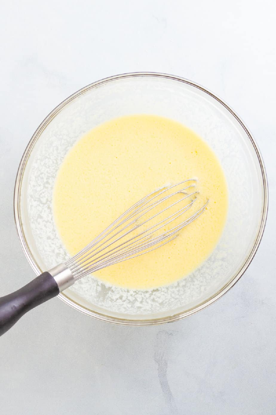 Wet ingredients in a bowl on a counter from overhead being mixed with a whisk.