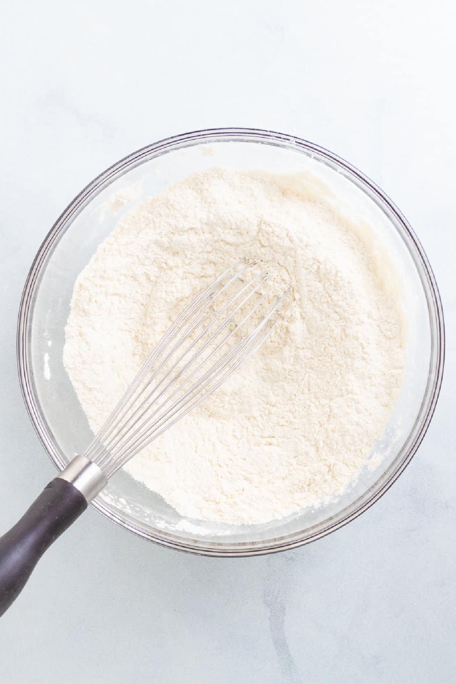 Flour and other dry ingredients in a bowl from above on a counter with a whisk mixing.
