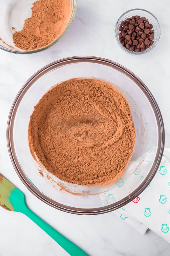 Mixing dry ingredients in a large mixing bowl with a spatula from above with a bowl of chocolate chips nearby on the counter.
