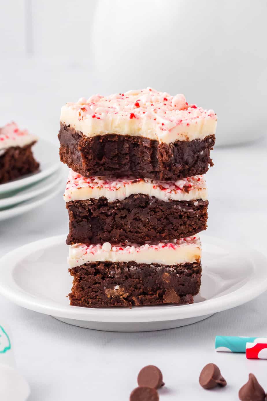 Peppermint bark brownies stacked three high on a plate from the side on a counter with a bite missing from the top brownie.