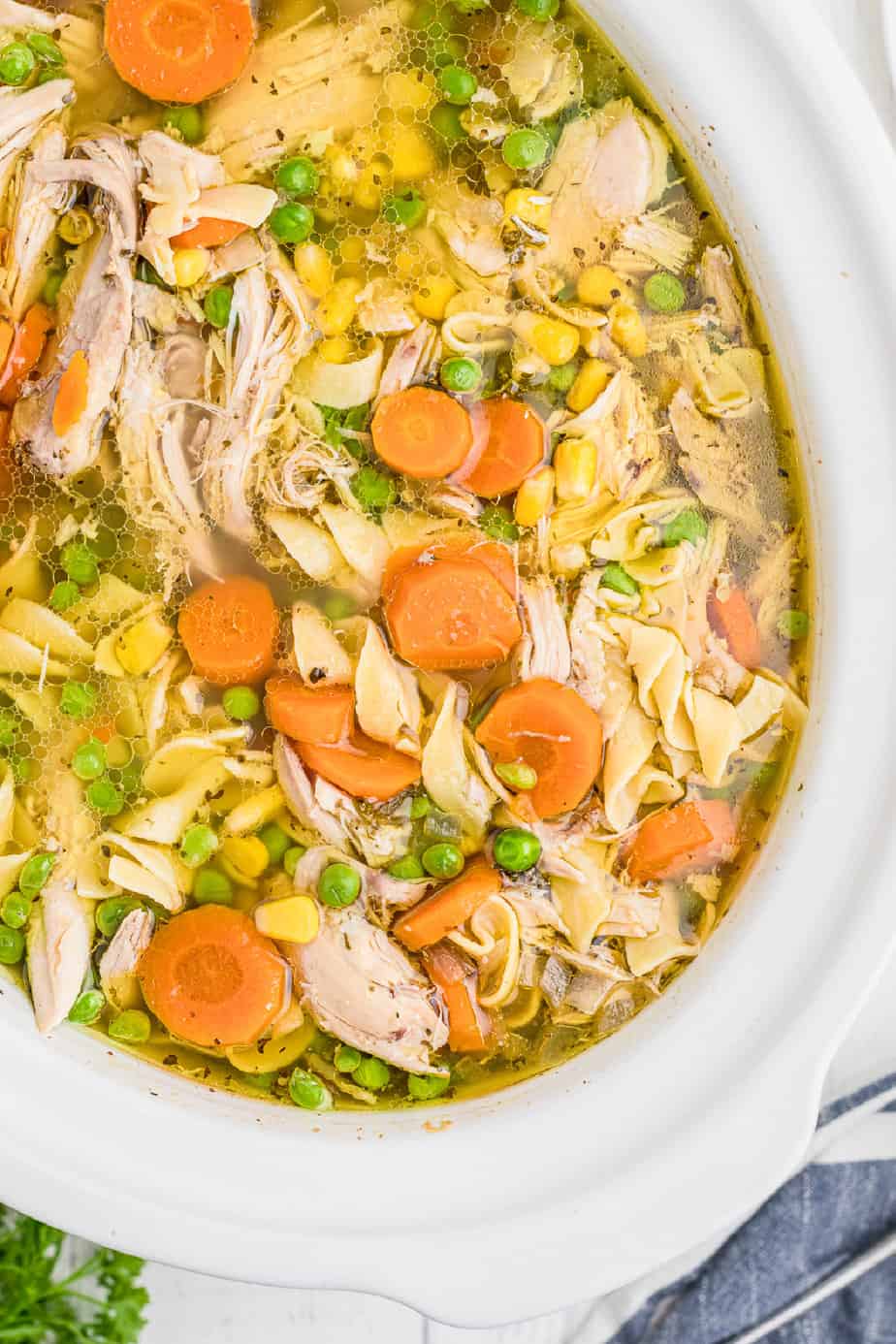 Overhead view of a full pot of chicken noodle soup packed with carrots, shredded chicken, corn and noodles sitting on a counter.