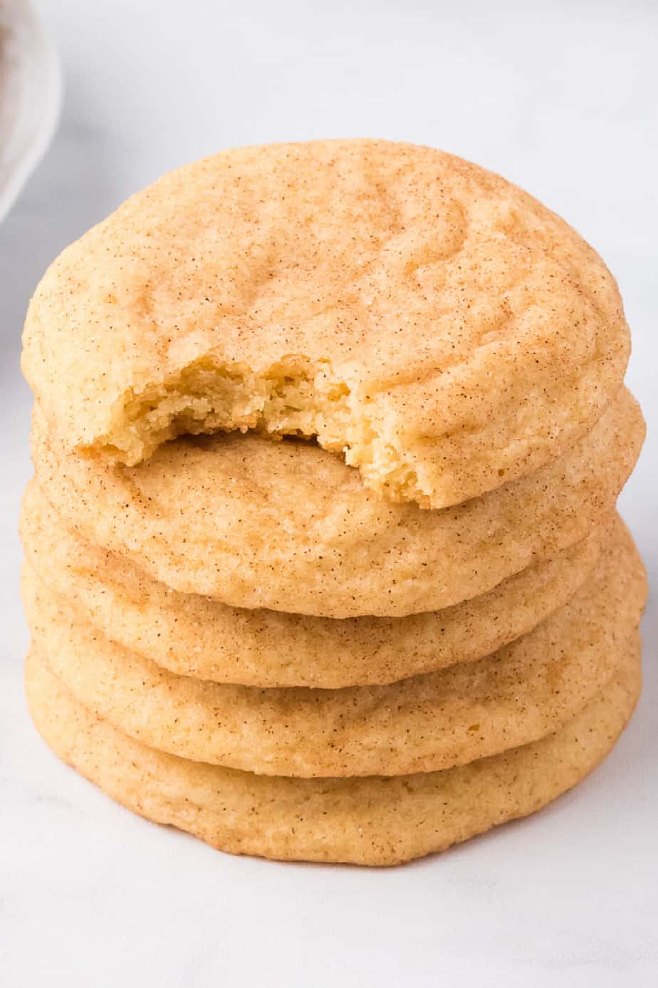Stack snickerdoodle cookies with a bite missing from the top cookie from an angle on a white counter.