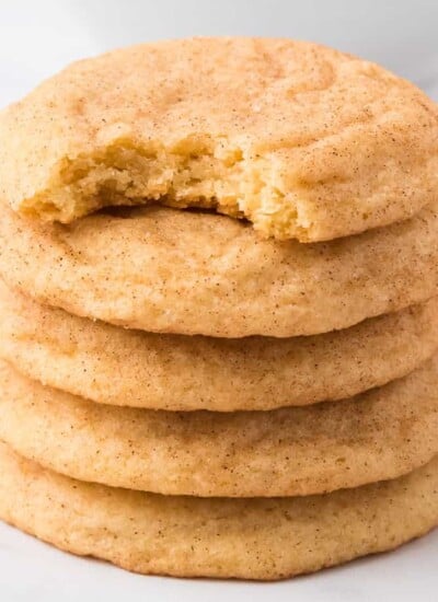 Stack of snickerdoodle cookies from the side on a white counter five cookies tall with the top cookie missing a bite.