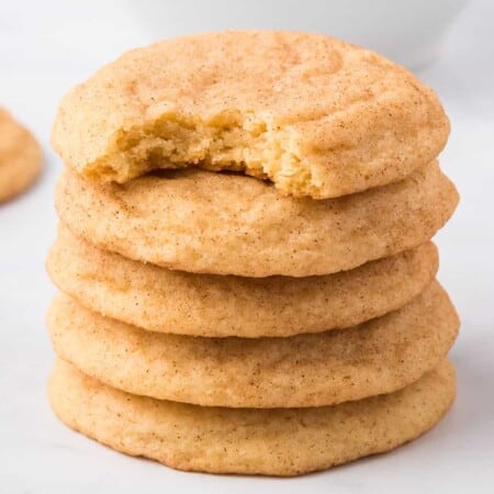 Stack of snickerdoodle cookies from the side on a white counter five cookies tall with the top cookie missing a bite.