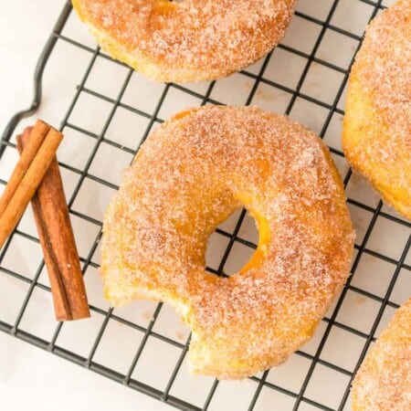 Three cinnamon sugar coated biscuit dough donuts cooling on a wire rack on a counter from above with one donut missing a bite.