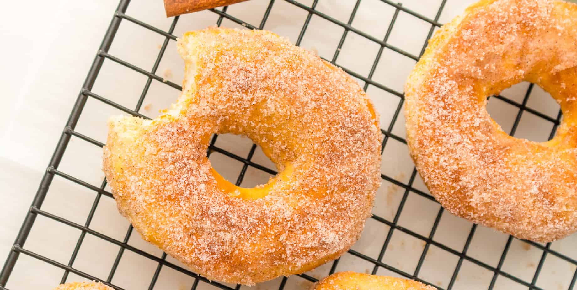 Two sugared donuts on a wire rack, one missing a bite.