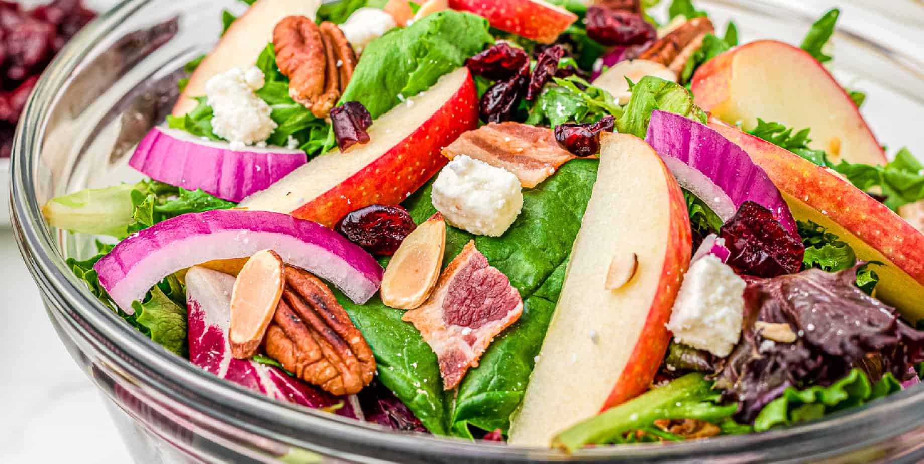 Apple cranberry salad in a large clear bowl from the side at a wide angle.