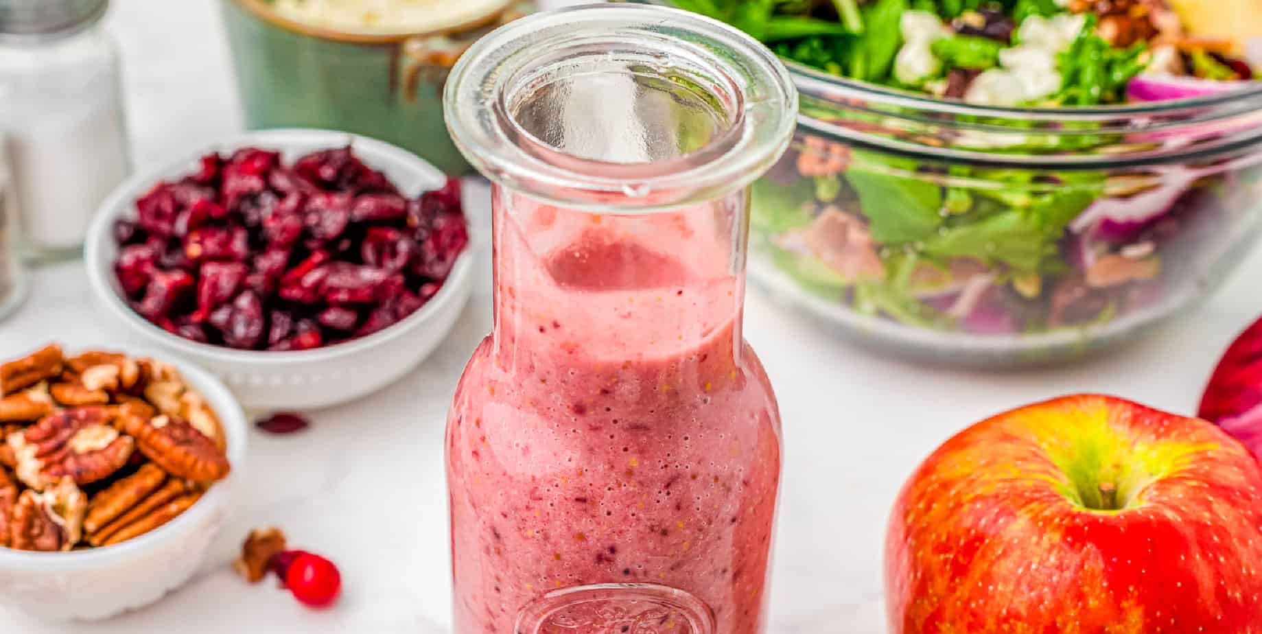 Cranberry vinaigrette dressing on a table with salad and other salad topping ingredients.