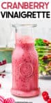 Tall close up side view of a glass bottle full of cranberry vinaigrette with salad in a bowl behind and title text overlay across the top.