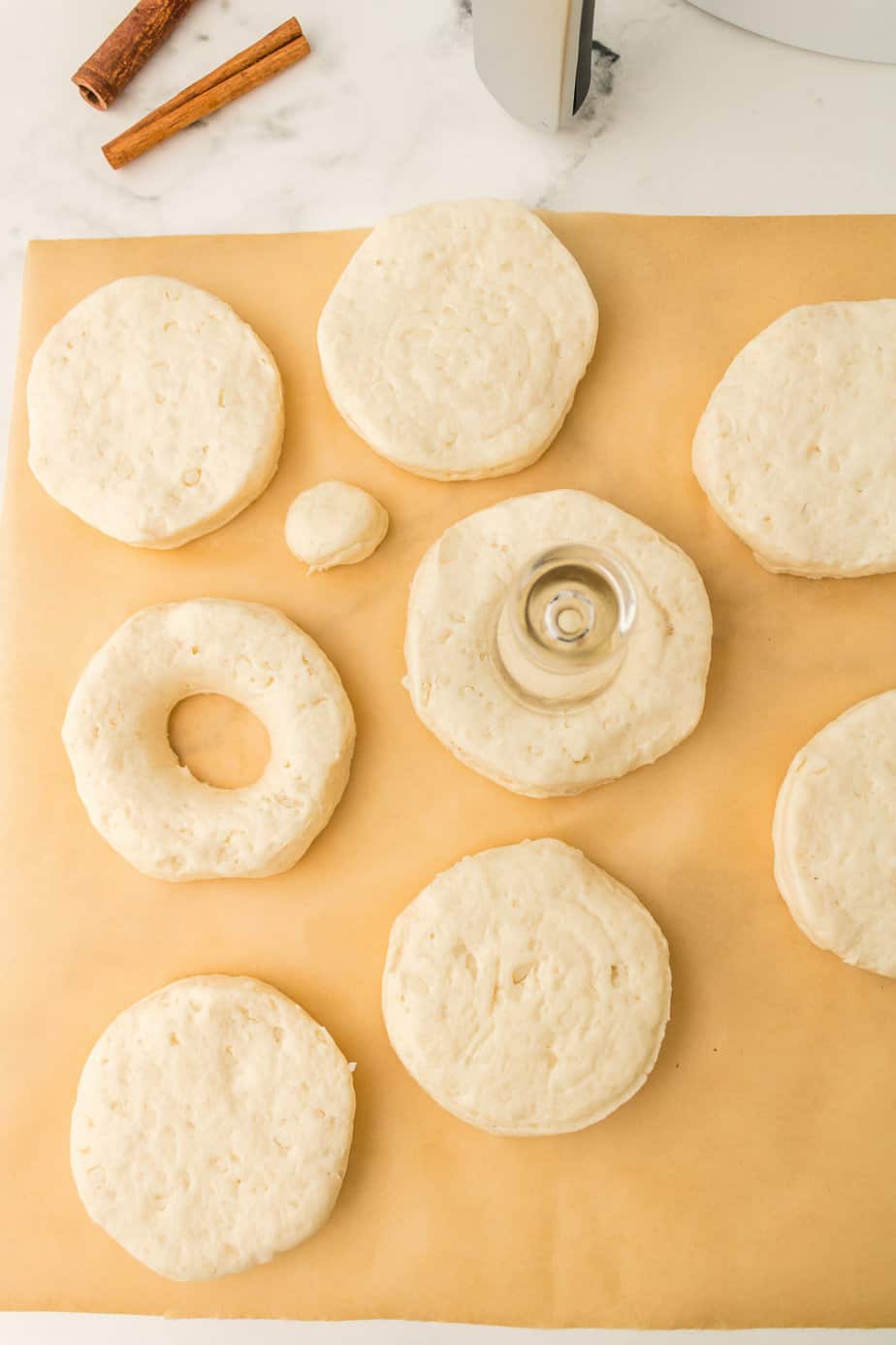 Slicing refrigerated biscuit dough pieces into round donuts with a whole in the center on a cutting board from above on a counter.