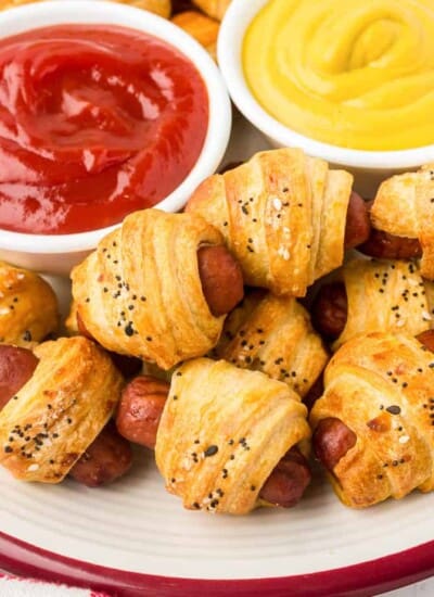 Pigs in a blanket on a plate from above with bowls of ketchup and mustard on the plate.
