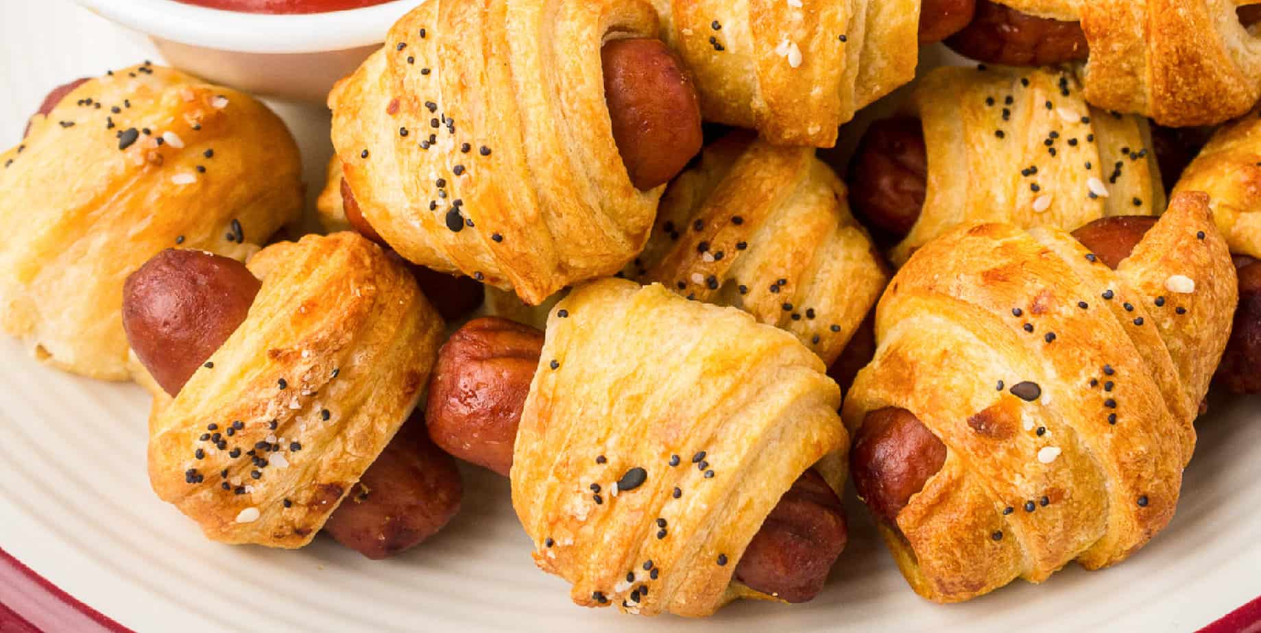 Pigs in a blanket on a plate piled from above with a wide view.