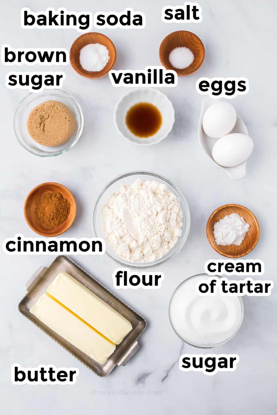 Ingredients for snickerdoodle cookies on a counter in bowls from overhead with labels.