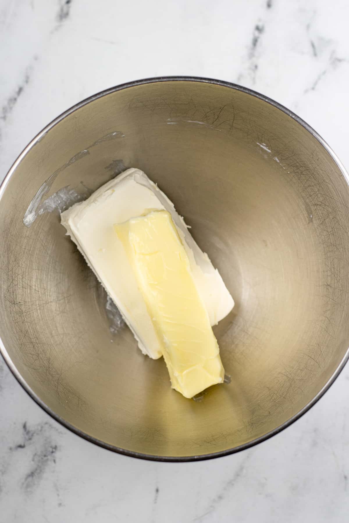 Butter and cream cheese in a mixing bowl from above on a counter.