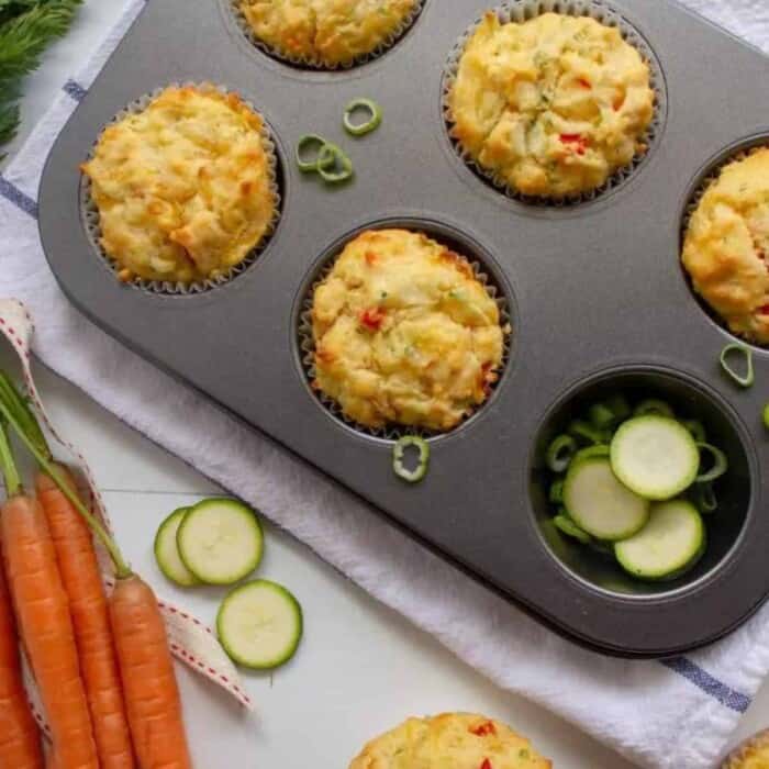 muffins with vegetables and cheese in them in a muffin tray on top of a white tea towel from above.