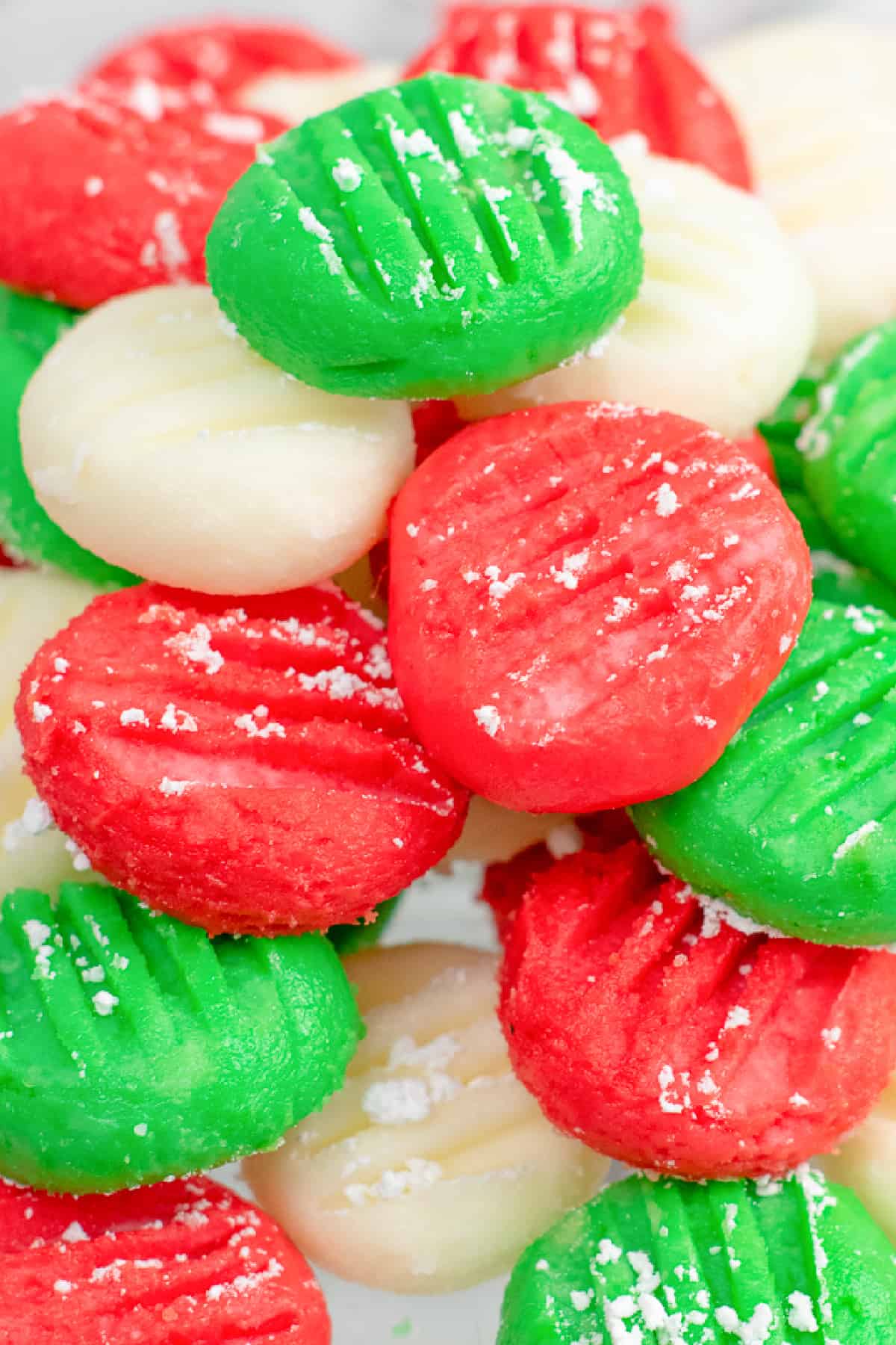 A close up view of a stack of white, green and red cream cheese mints in little disks piled on top of each other.