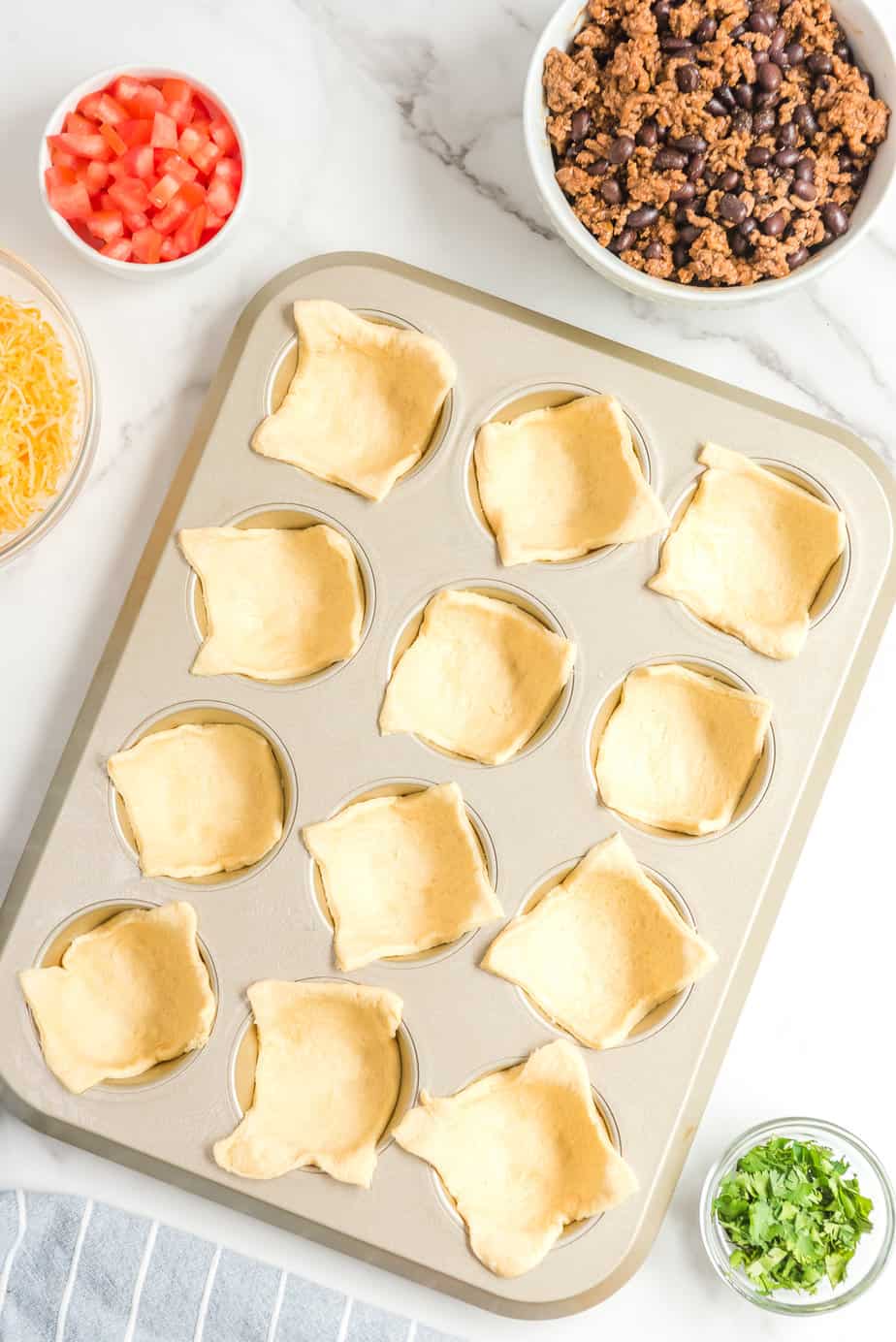 Crescent dough pieces place in a muffin tin on a counter from above.