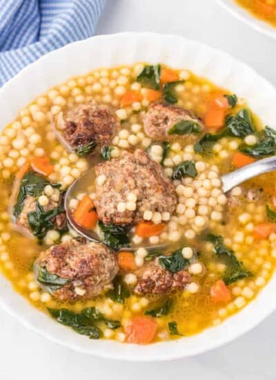 Italian wedding soup in a bowl on a counter from overhead full of meatballs, pasta and vegetables being lifted by a spoon.