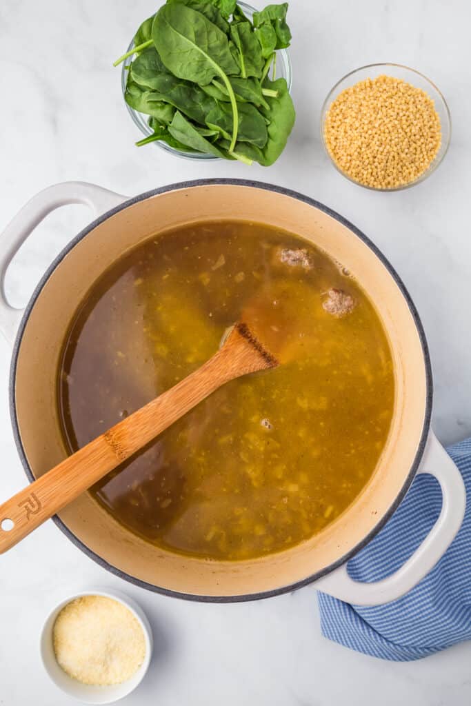 Cooking broth for italian wedding soup with spinach, pasta and parmesan cheese on the counter nearby from overhead.
