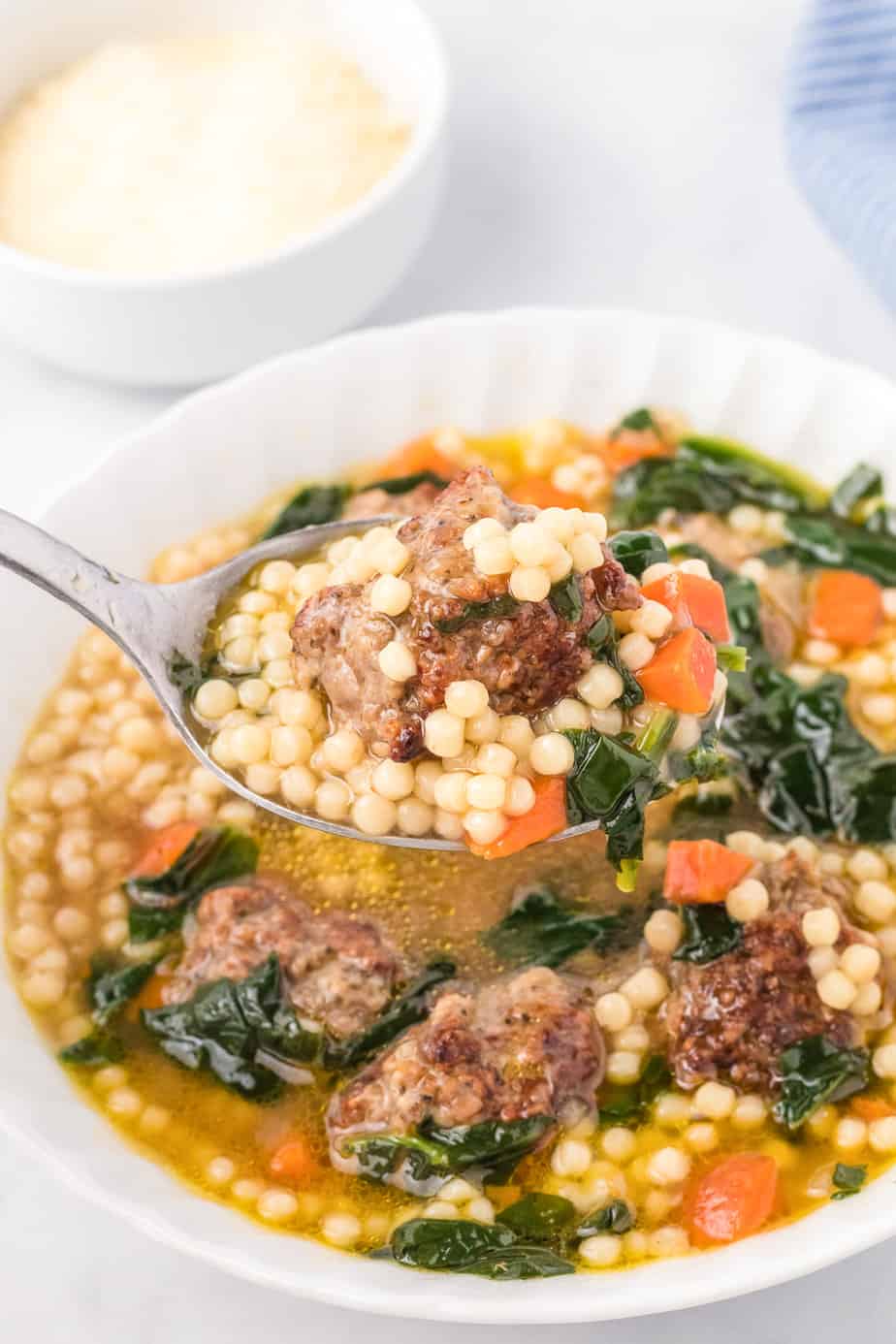 A spoonful of meatball, spinach and tiny pasta being scooped from a bow of wedding soup.