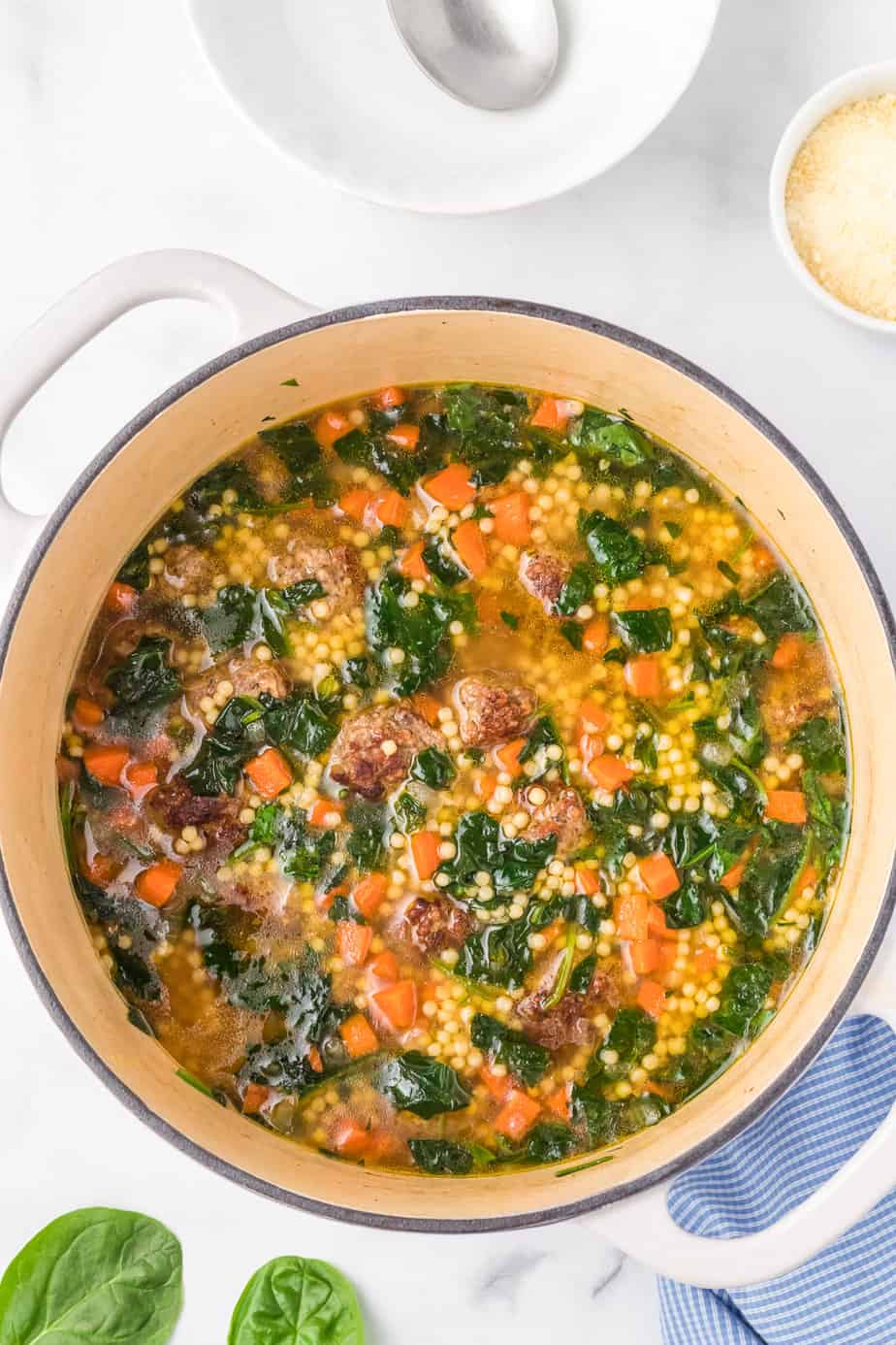 Italian wedding soup in a pot from overhead on a counter with chopped spinach, carrots, meatballs and pasta in the soup from overhead.