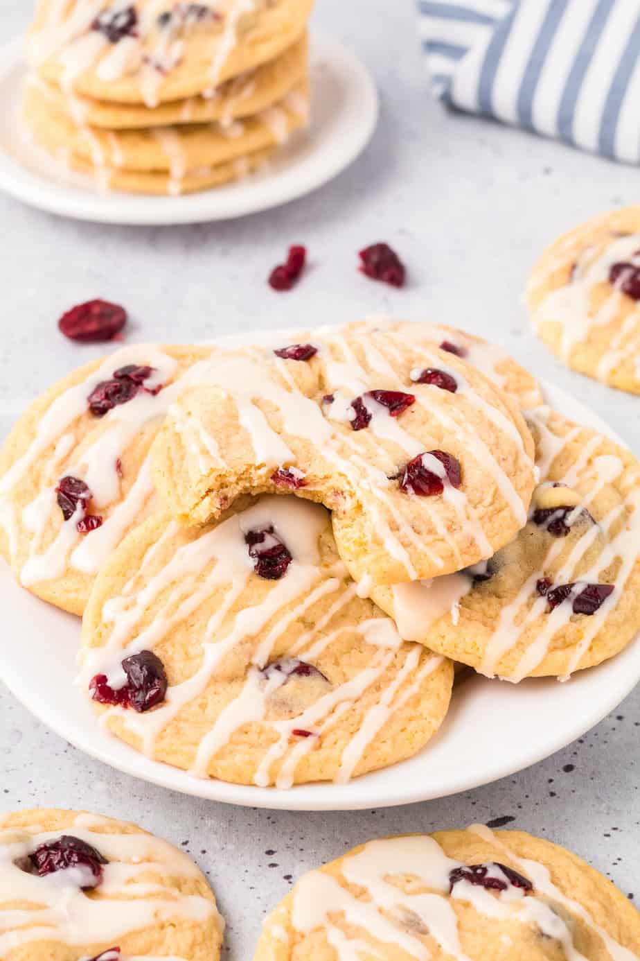 Cookies stacked on a plate on a counter topped with cranberries and glaze, with the top cookie missing a bite.