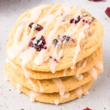 Stacked cookies with cranberries on top and drizzled white glaze stacked on a counter.