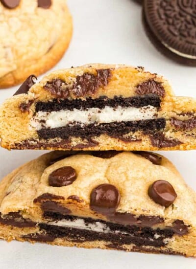 Up close view of a chocolate chip cookie cut in half showing an Oreo in the middle with more cookies on the counter nearby.