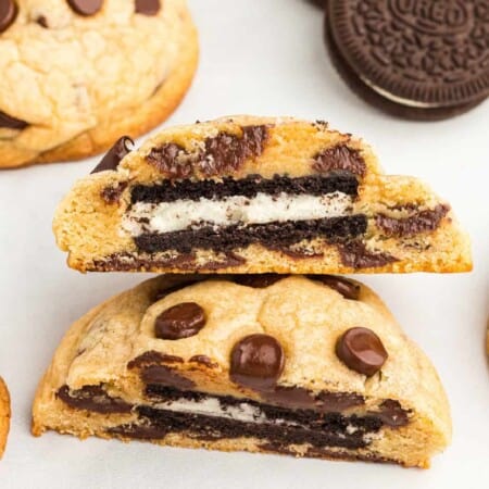 Up close view of a chocolate chip cookie cut in half showing an Oreo in the middle with more cookies on the counter nearby.