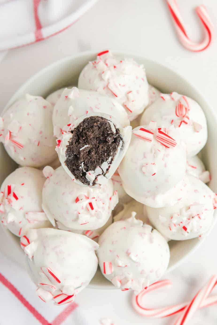 Peppermint Oreo balls in a bowl from overehead on a counter with more candy canes on the counter nearby and one truffle missing a bite.