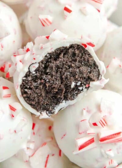 Peppermint Oreo Balls stacked close up with one missing a bite that shows brown chocolate inside the white outside topped with peppermint.