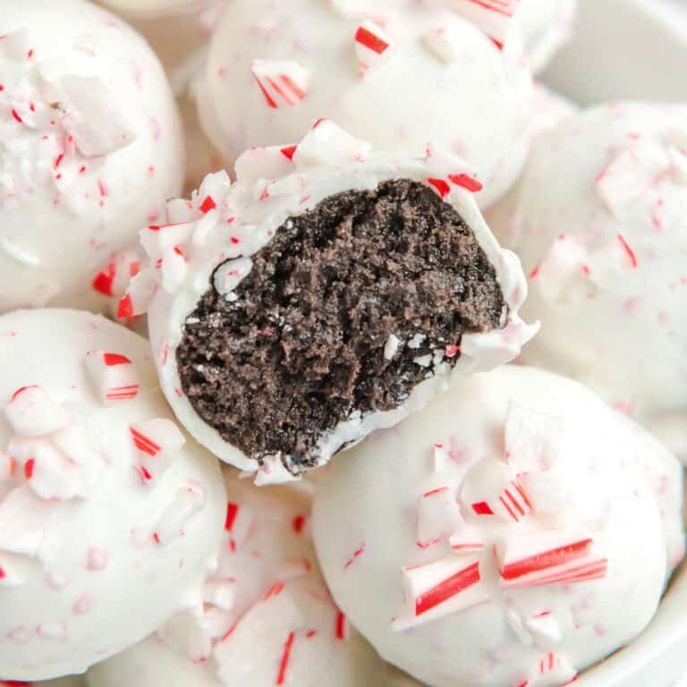 Peppermint Oreo Balls stacked close up with one missing a bite that shows brown chocolate inside the white outside topped with peppermint.