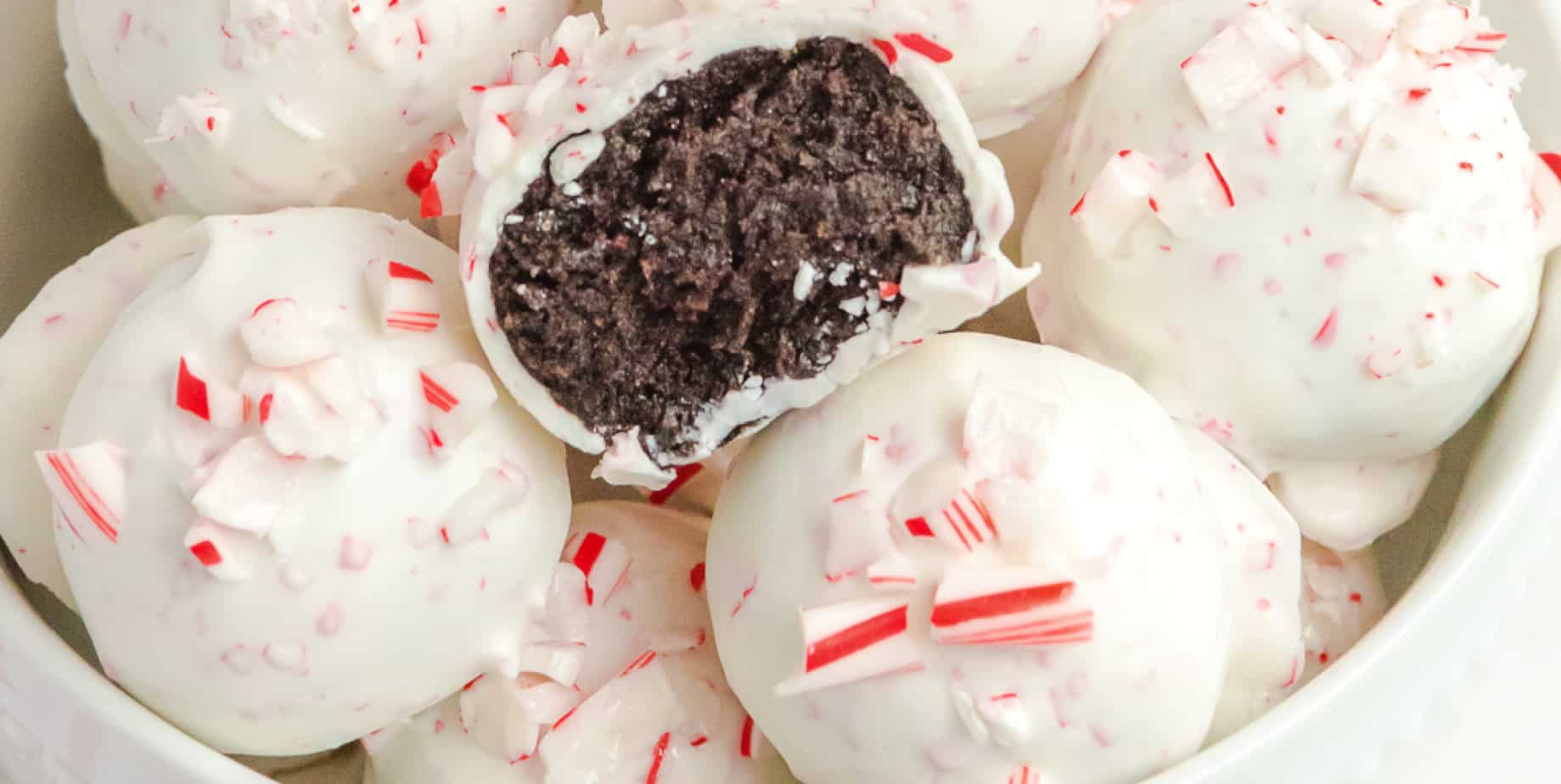 Peppermint candy cane oreo balls dipped in white chocolate close up wide in a bowl with one truffle missing a bite.