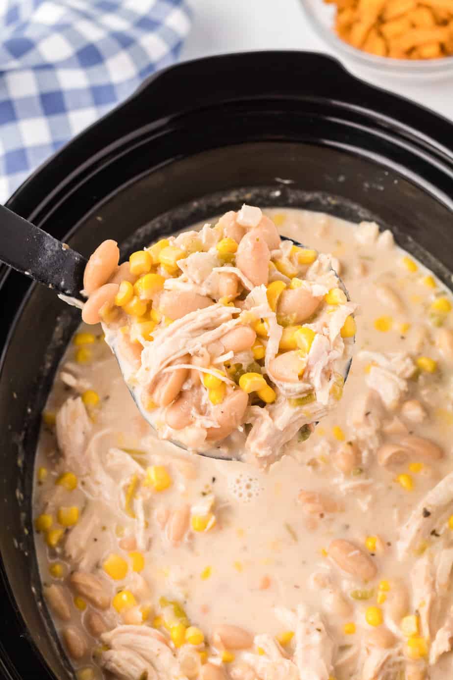A scoop of creamy chicken tortilla soup being lifted with a ladle up close from a slow cooker.