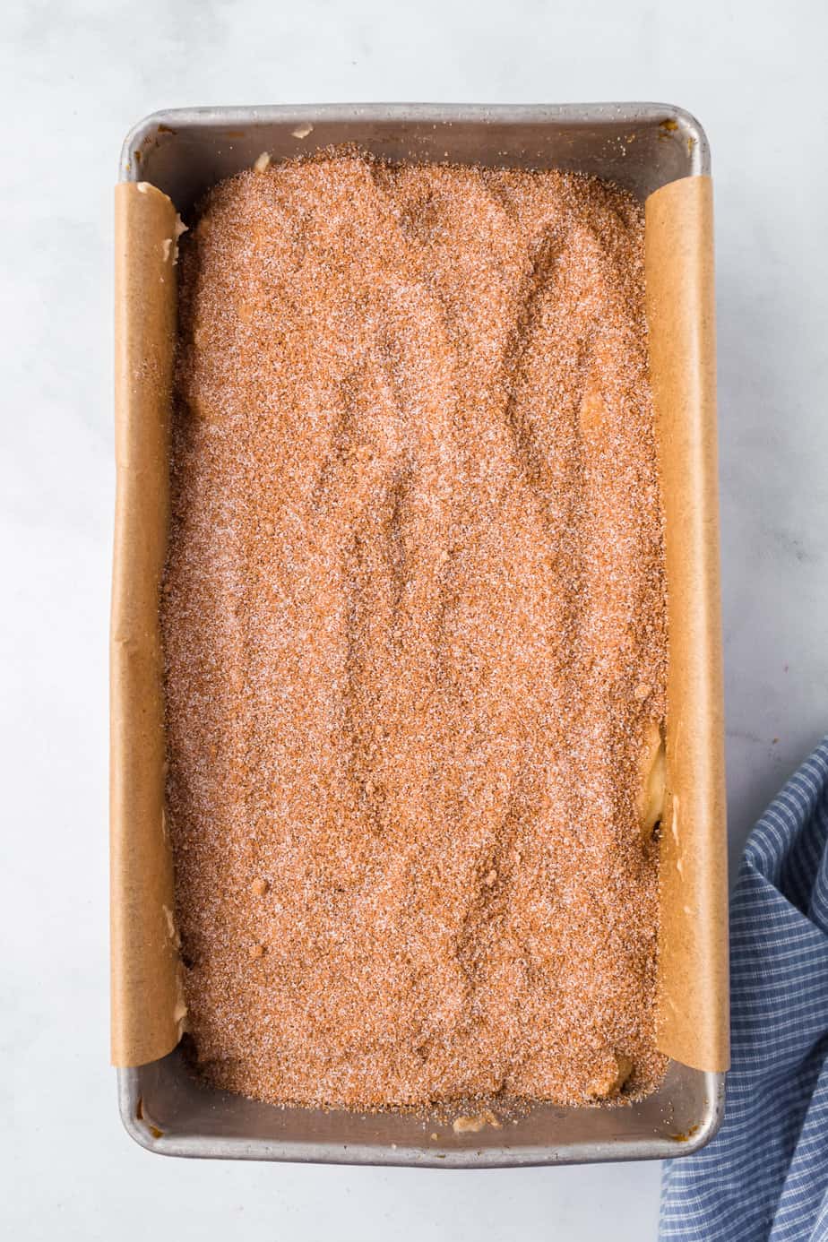 Layered batter topped with cinnamon sugar in a loaf pan from above on a counter.
