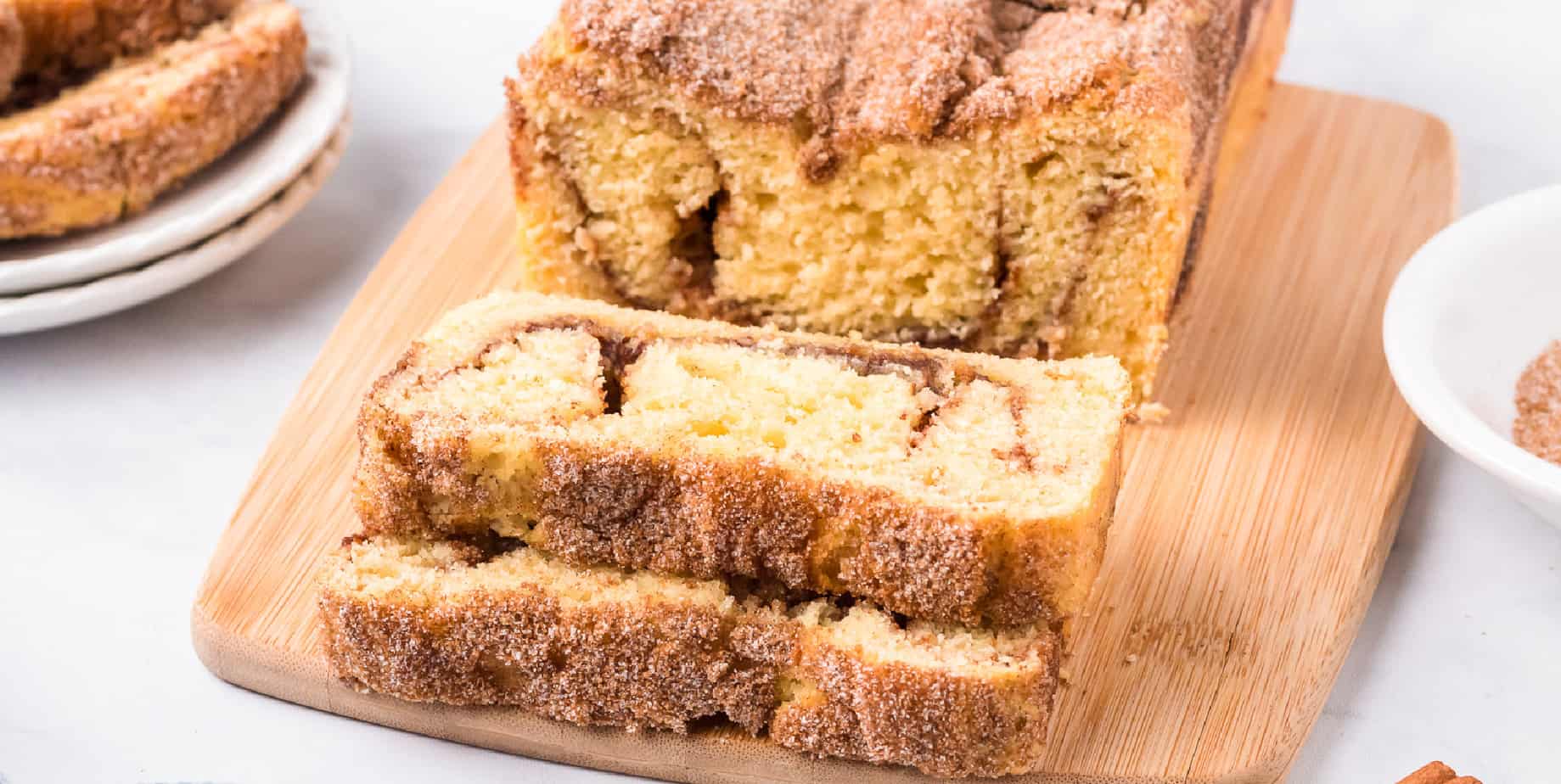 Snickerdoodle bread on a cutting board with two slices cut from the loaf on a counter.