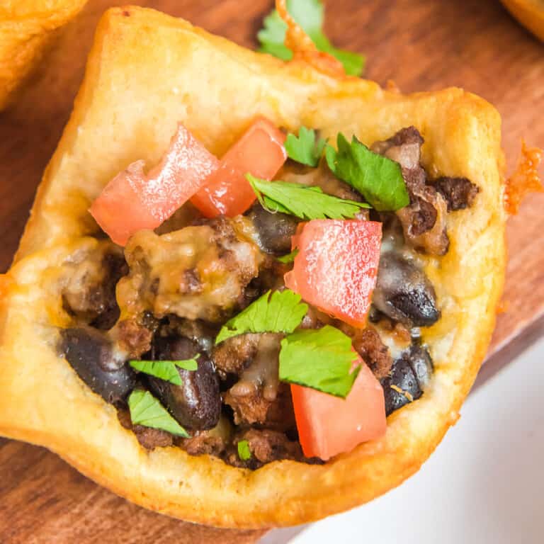 Close up overhead of a taco cup full of ground meat, beans, tomatoes and cilantro.