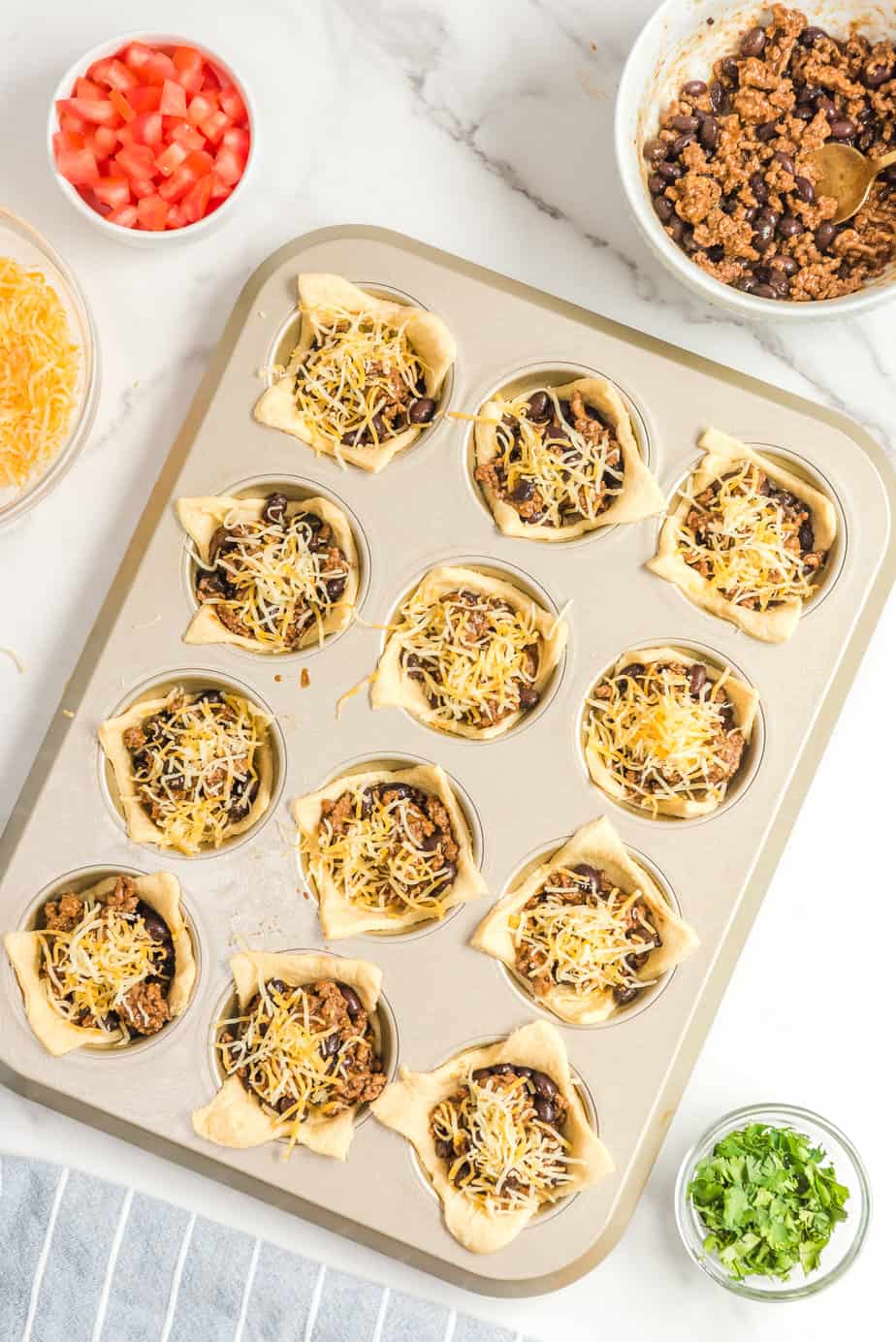 Beef, beans and cheese added to dough in muffin tins from above.