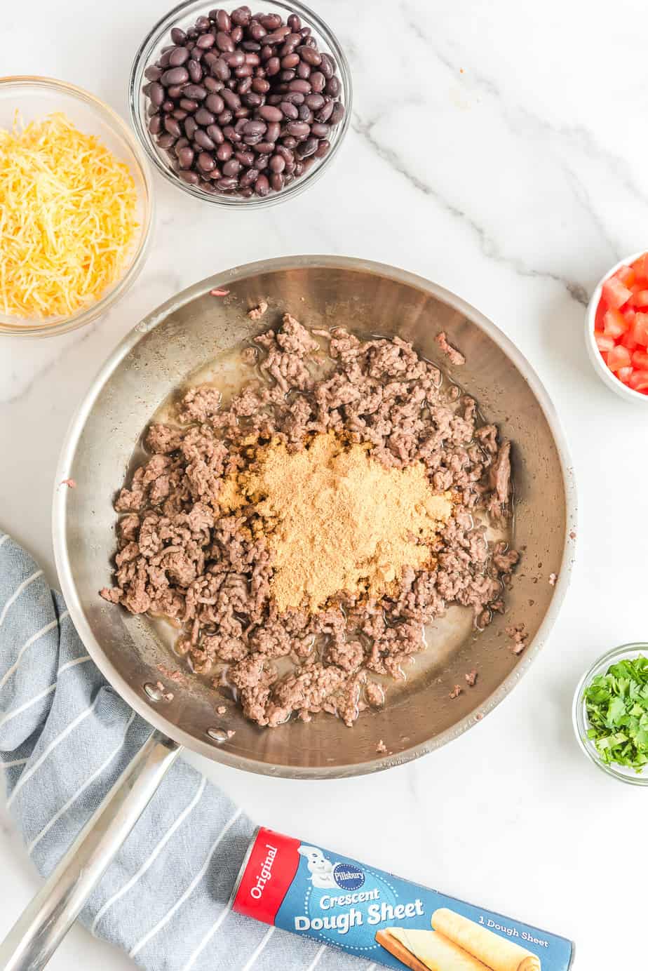 Taco seasoning and water being added to browned ground beef in a pan from overhead.