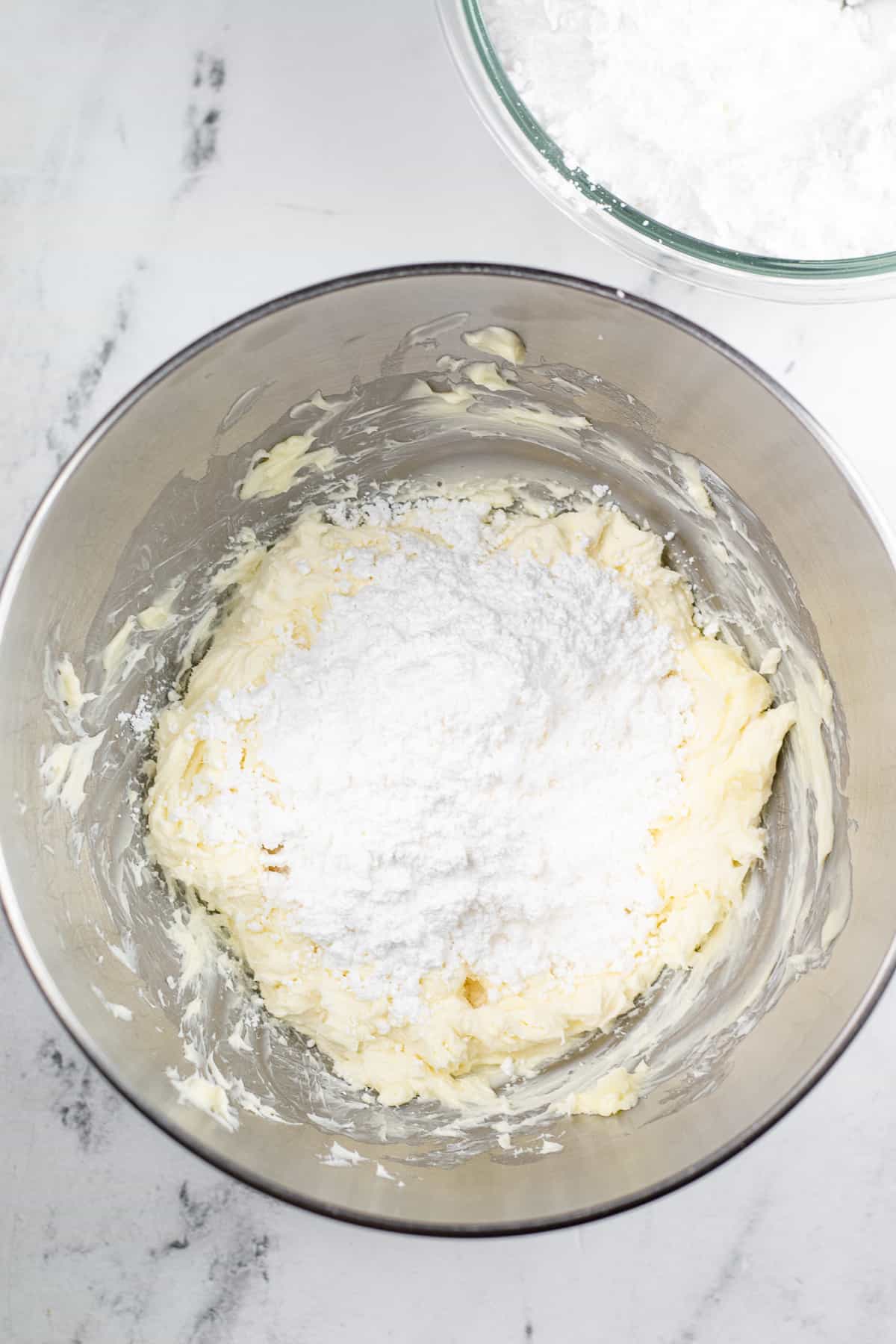 Mixing powdered sugar into a butter cream cheese mixture in a mixing bowl on a counter from overhead.