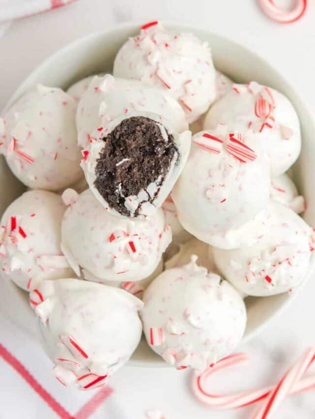 Peppermint Oreo balls in a bowl from overehead on a counter with more candy canes on the counter nearby and one truffle missing a bite.