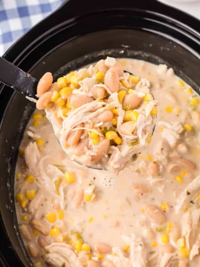 A scoop of creamy chicken tortilla soup being lifted with a ladle up close from a slow cooker.