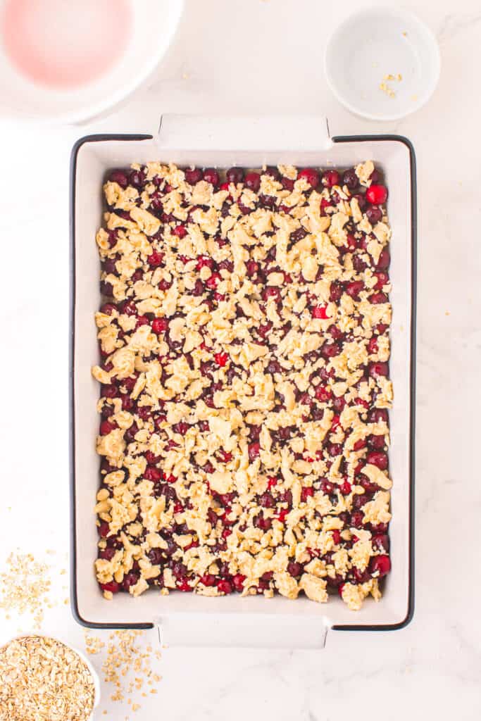 Dough crumbled across the top of the cranberry mixture in a large rectangular pan from overhead on a counter.