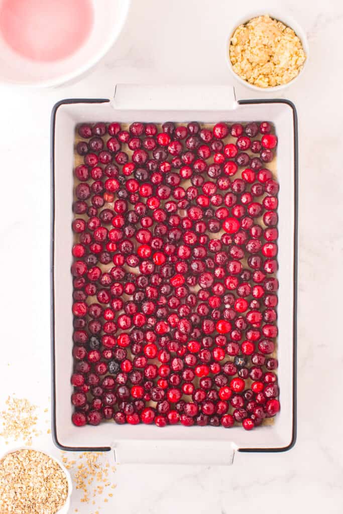 Cranberry mixture layered in a large rectangular pan from overhead on a counter with more dough in a bowl nearby.