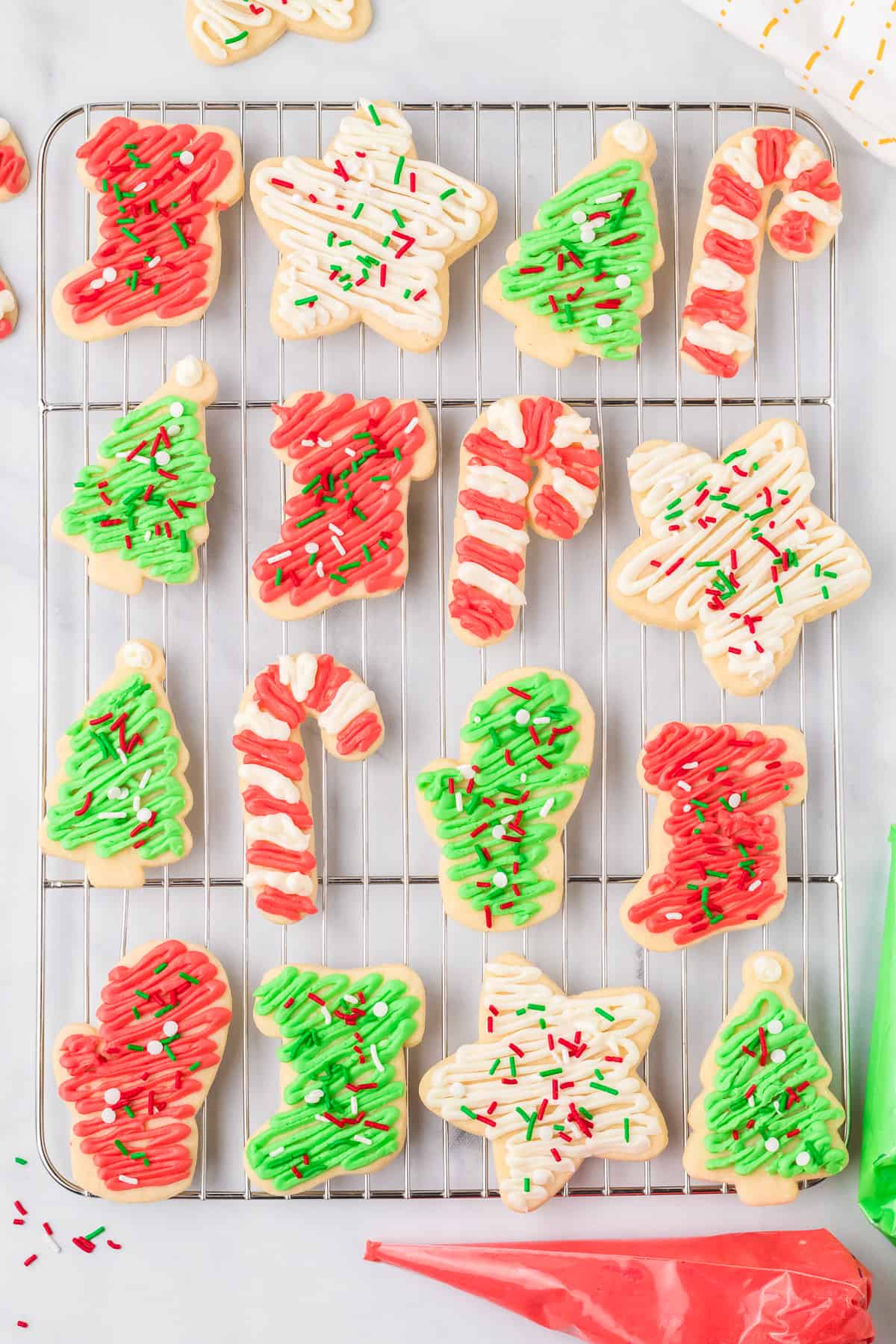 Sugar cookies frosted in red, white and green frosting on a wire cooling rack from overhead on a counter.