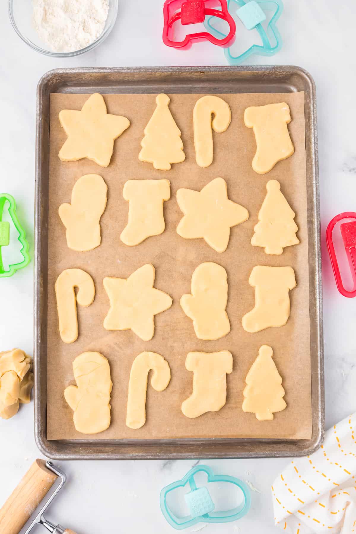 Sugar cookies cut out in candy canes, stars, trees and other christmas shapes on a cookie sheet from above.