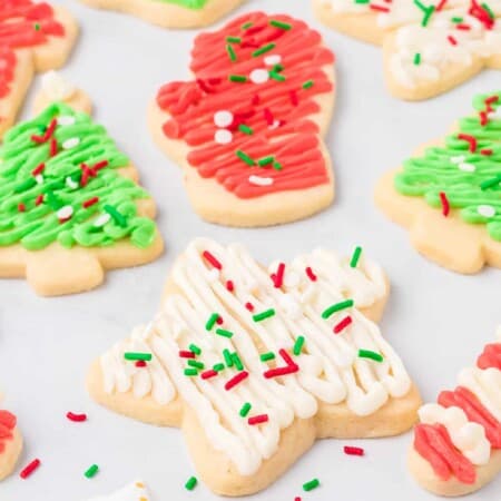 Frosted sugar cookies shaped like stars, Christmas trees and mittens frosted with red, green and white frosting and sprinkles from the side.