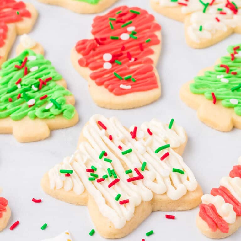 Frosted sugar cookies shaped like stars, Christmas trees and mittens frosted with red, green and white frosting and sprinkles from the side.