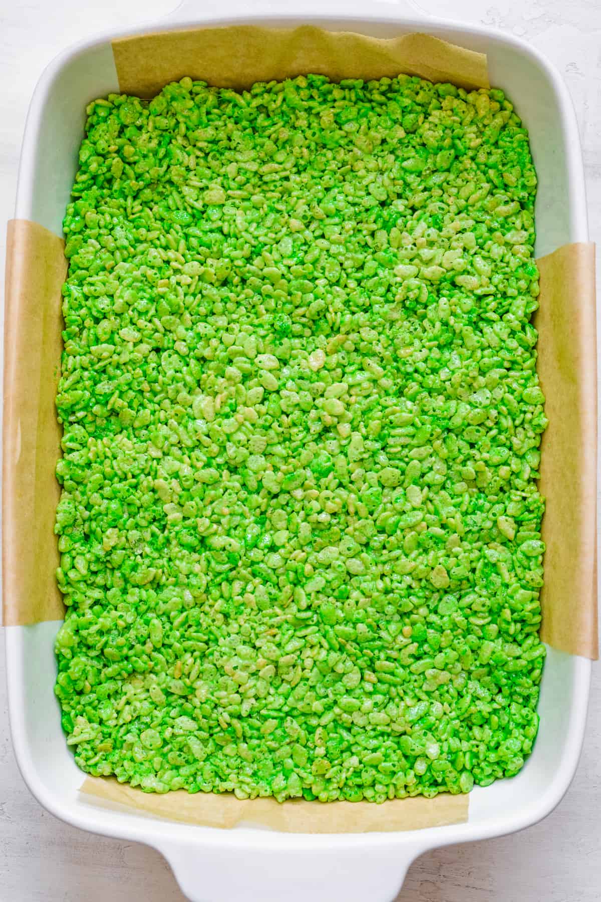 Green Rice Krispies treats in a large rectangular pan from overhead on a counter lined with parchment paper.